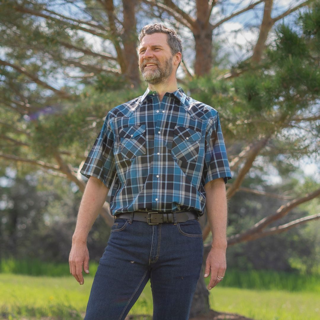 Men's short-sleeve plaid western shirt. Western shirt is teal, black and white with pearl snaps.